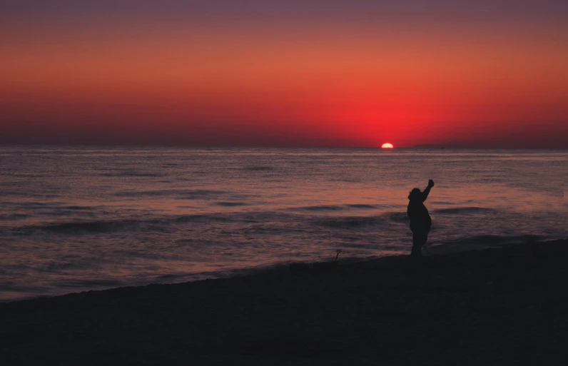 a person standing on top of a beach holding up a yellow frisbee