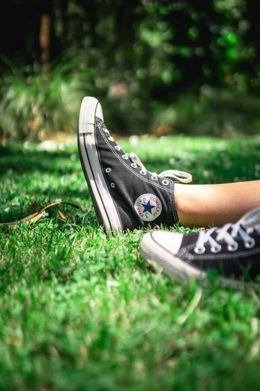 a person wearing a converse shoe and black sneakers standing on green grass