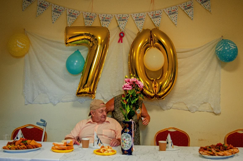 a man in a wheel chair sitting at a table with balloons and food