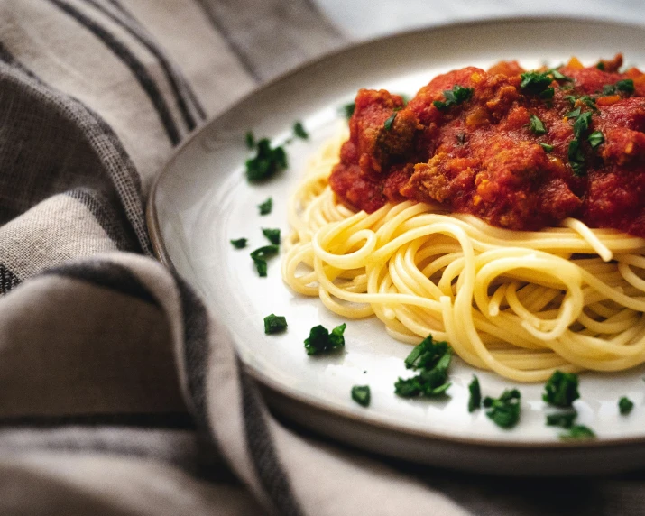 plate of spaghetti with sauce and parsley on cloth