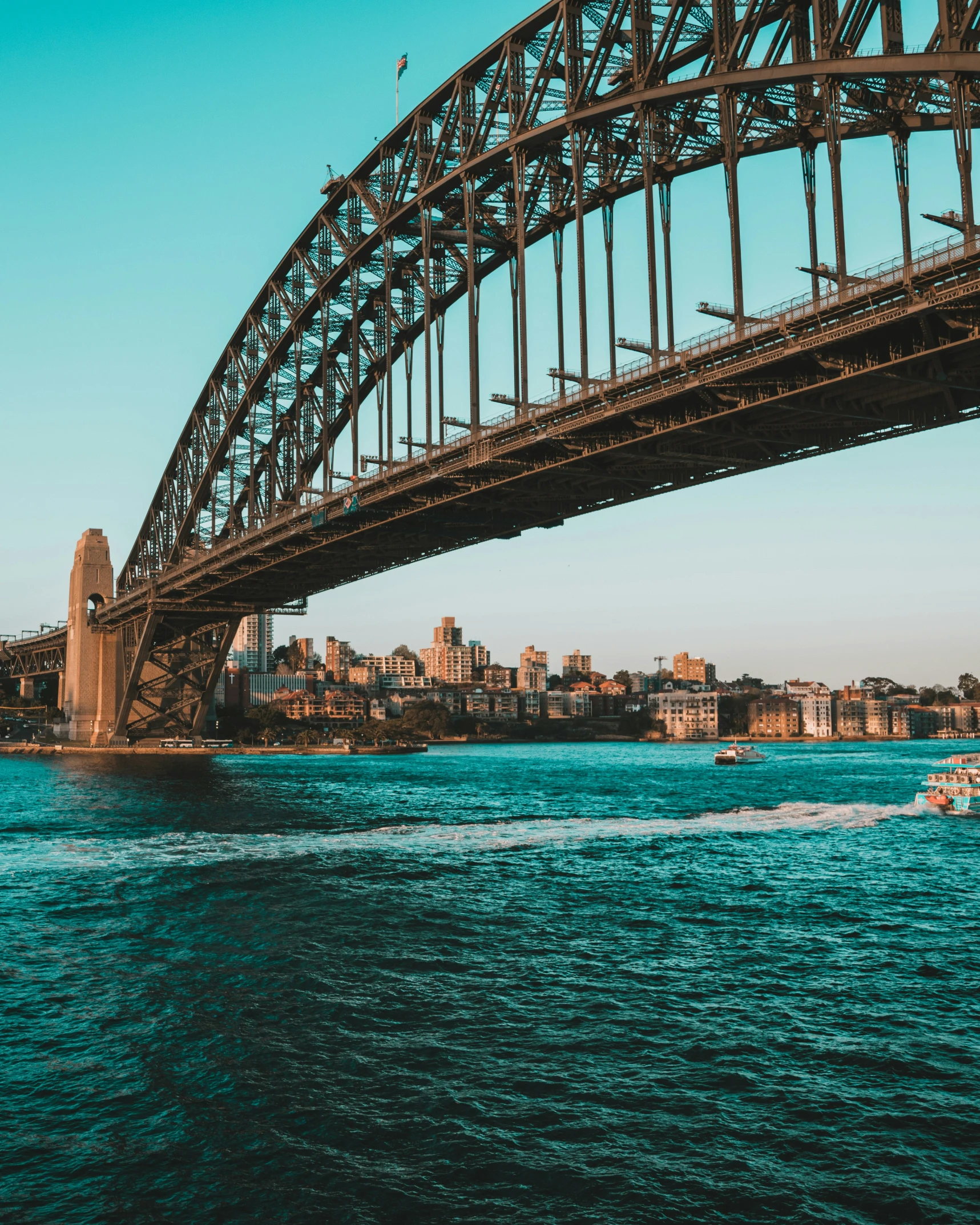 a boat rides through the blue water beneath the sydney bridge