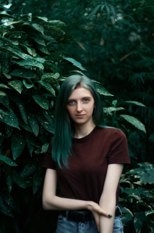 a woman with blue hair standing near a bush