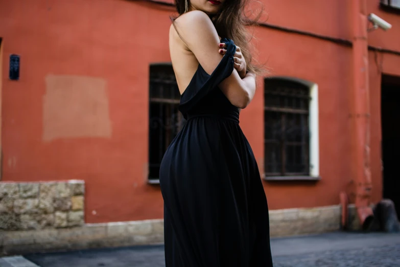 a woman in a black dress stands on a street