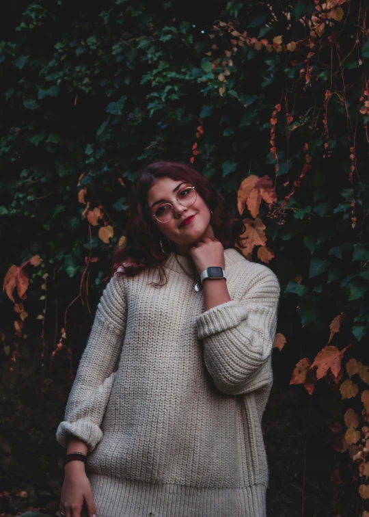 a woman wearing glasses stands in front of ivy covered trees