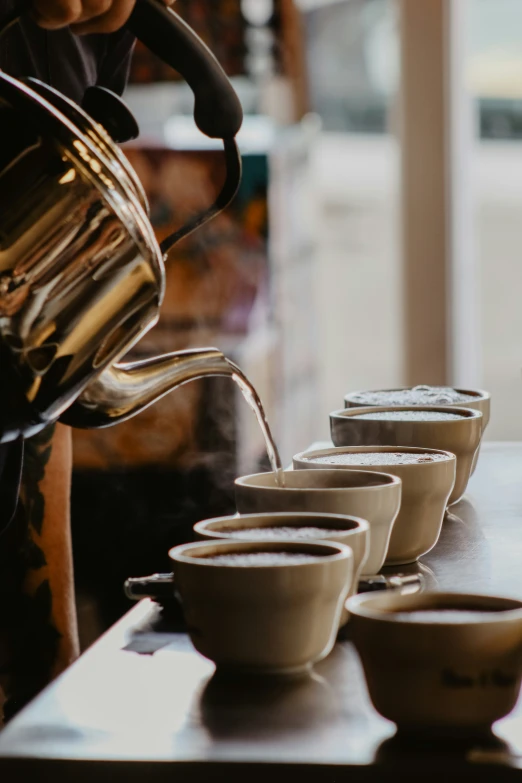 a line of small bowls being poured into a teapot