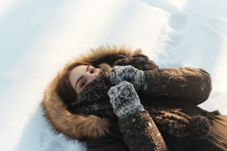 a girl covered in warm clothing lays on the snow with her eyes closed