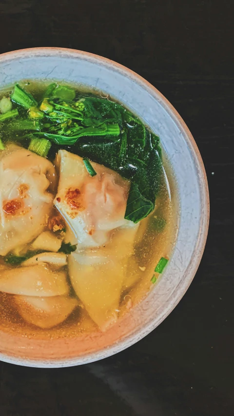 bowl of soup with soup dumplings and spinach in it