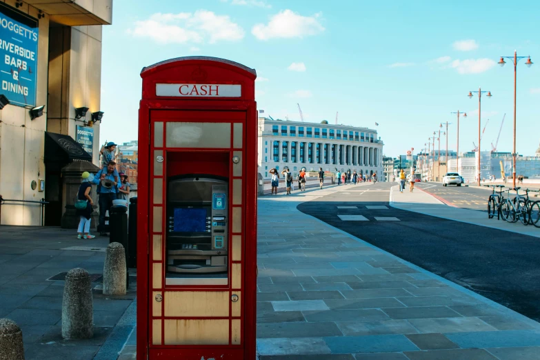 a red phone booth near the street with people waiting to see it