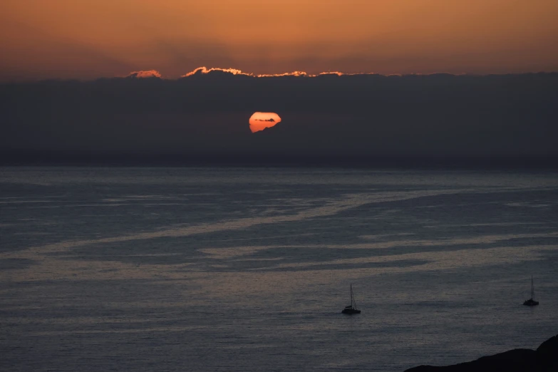 the sun rising over the ocean, with two small boats out on the water