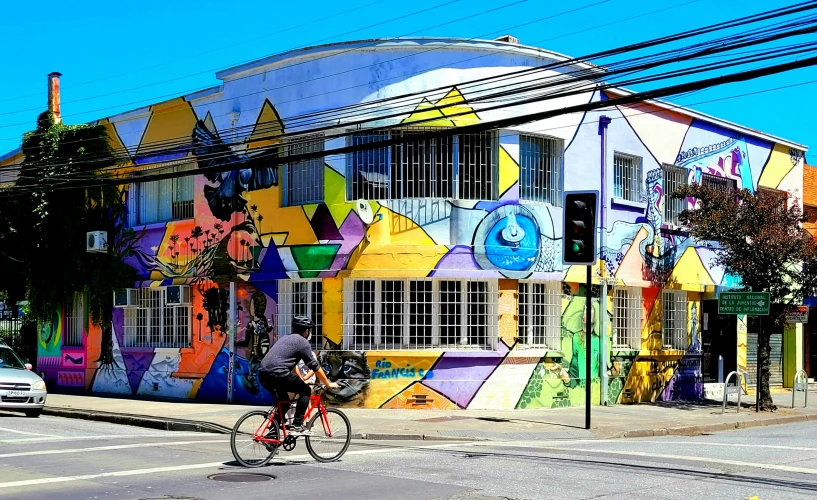 the bike rider is going past the large building painted with a colorful pattern