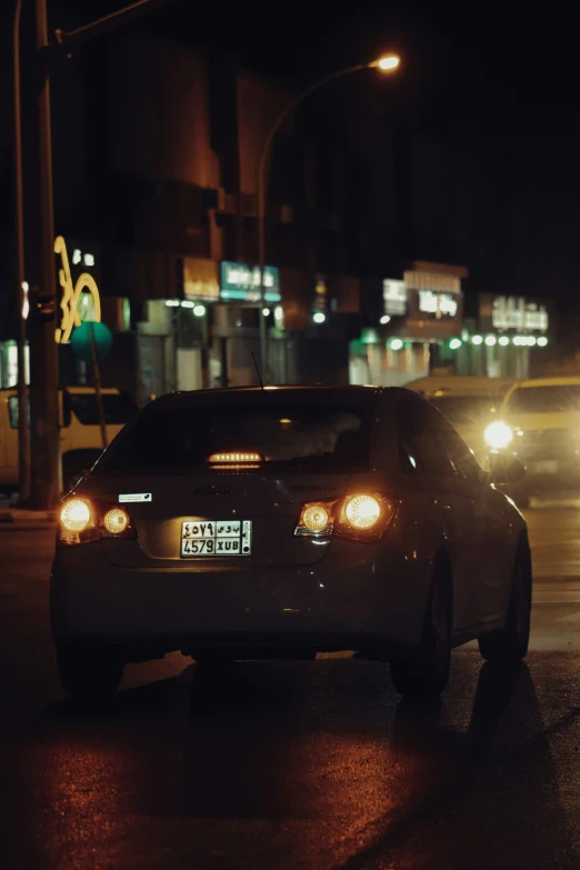 two cars sit side by side on a wet city street at night