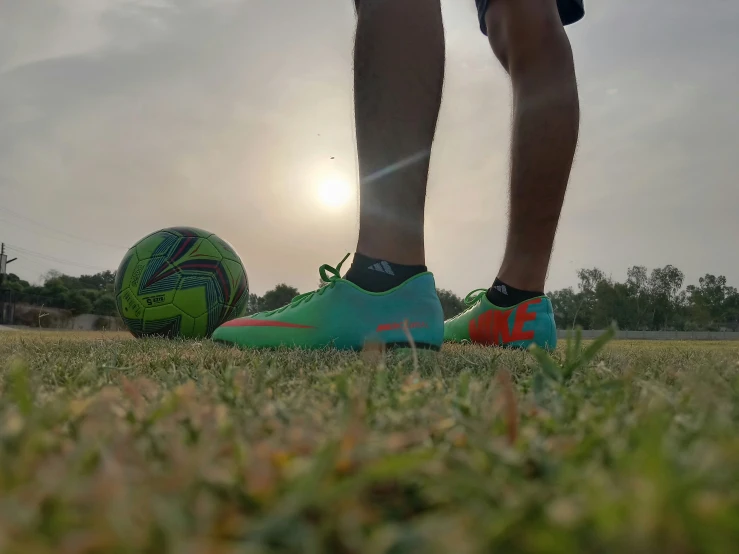 the legs of a man wearing green and orange soccer shoes next to a ball