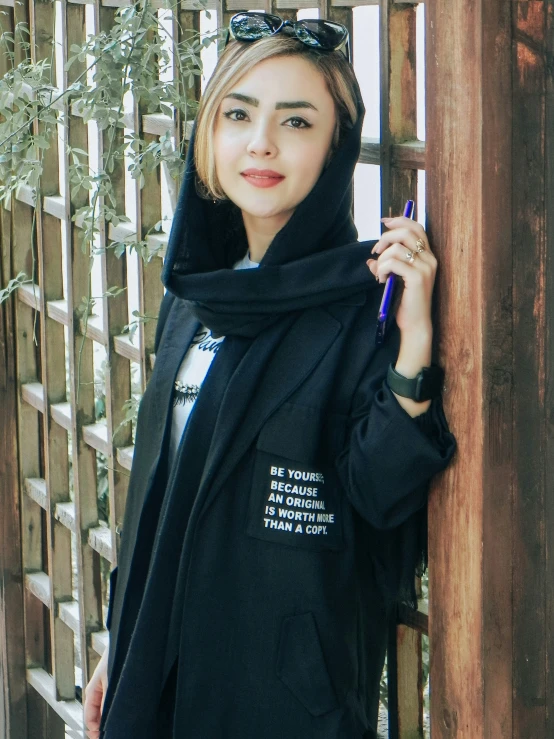 a young woman with her hoodie open, standing against a fence