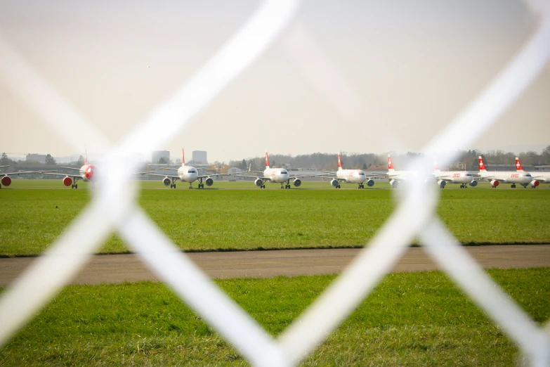 planes in a row on an airstrip seen through a fence