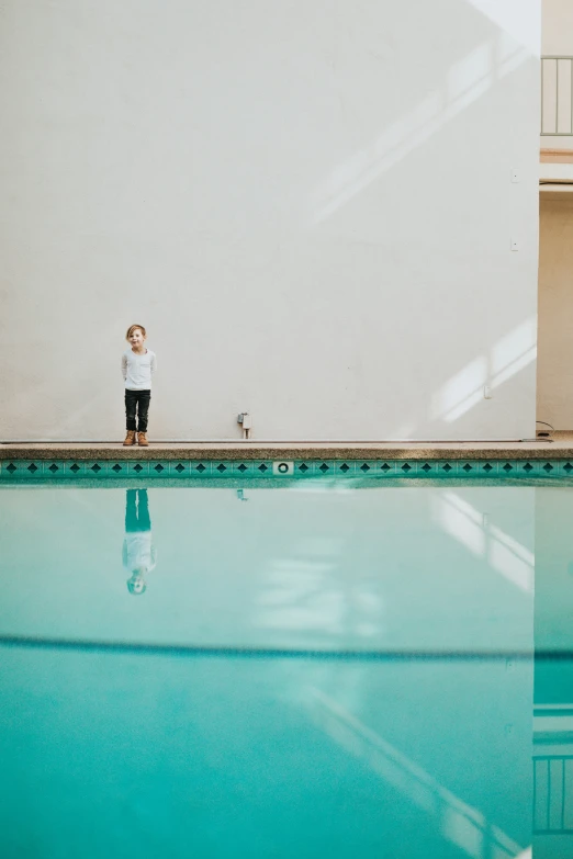 a boy standing on a step beside a swimming pool