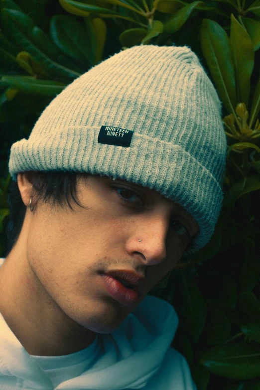 the young man in the beanie is sitting against the foliage