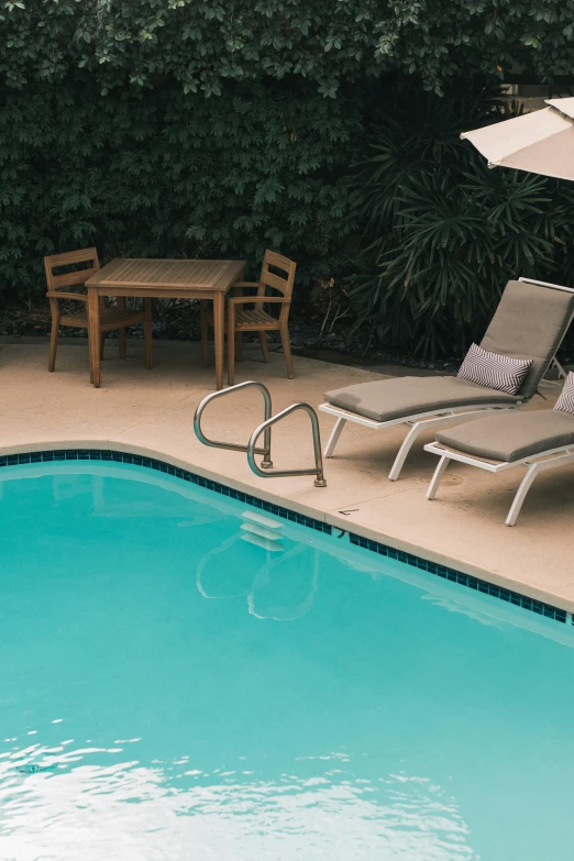two chairs near the edge of a pool and an umbrella