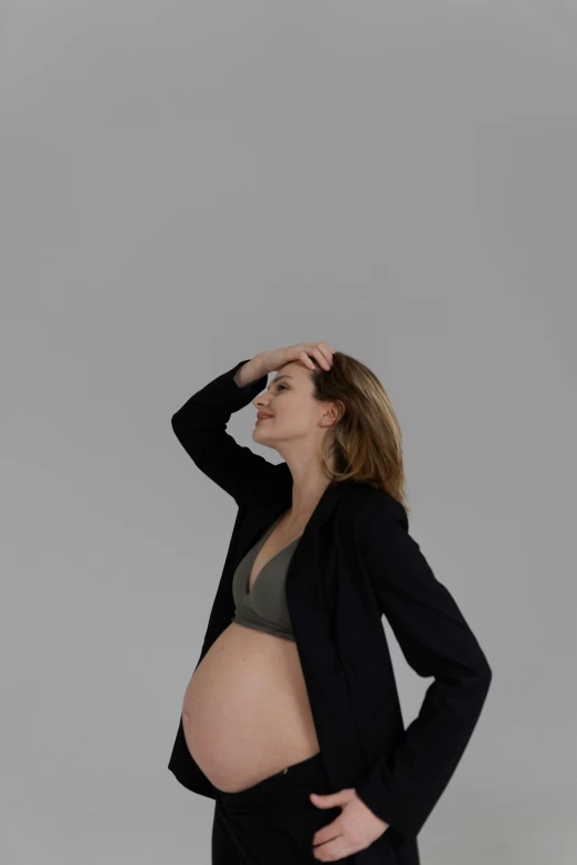 a pregnant woman standing in a dark suit and looking up