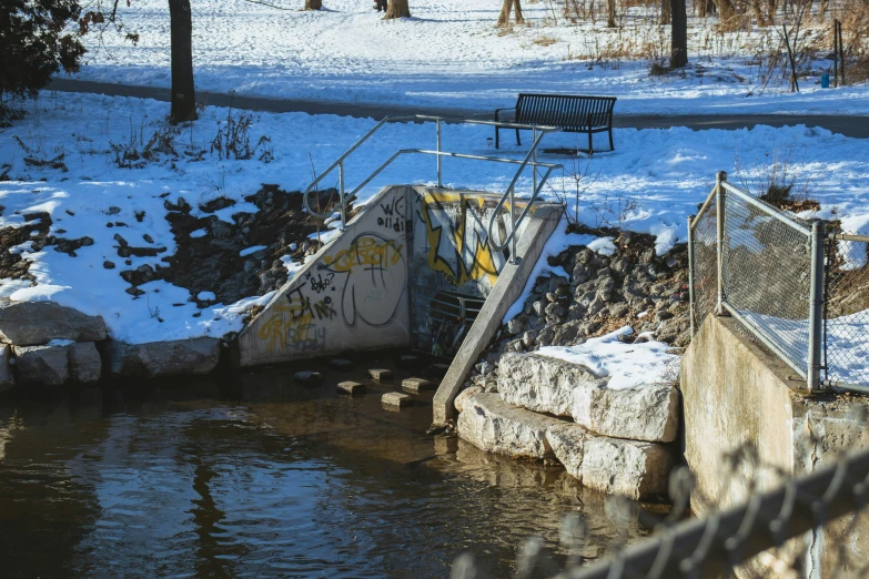 a bench by the river with snow on the ground