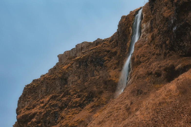 a waterfall with brown grass and a blue sky