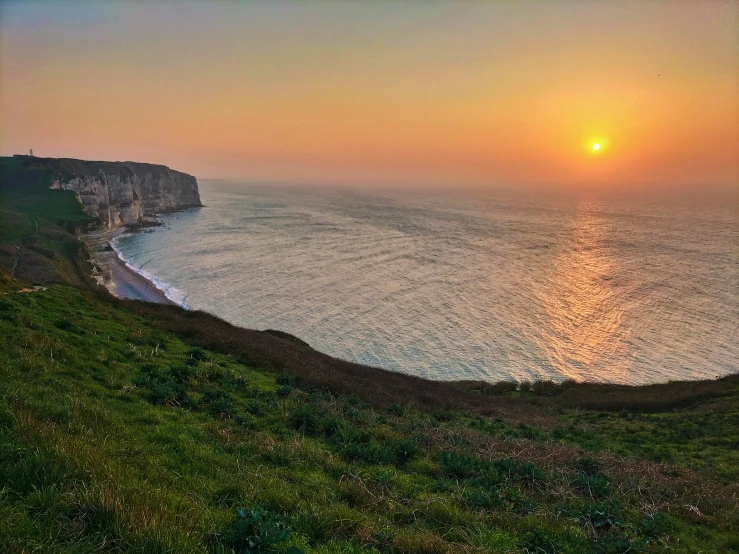 the sun sets over the ocean along a rocky cliff