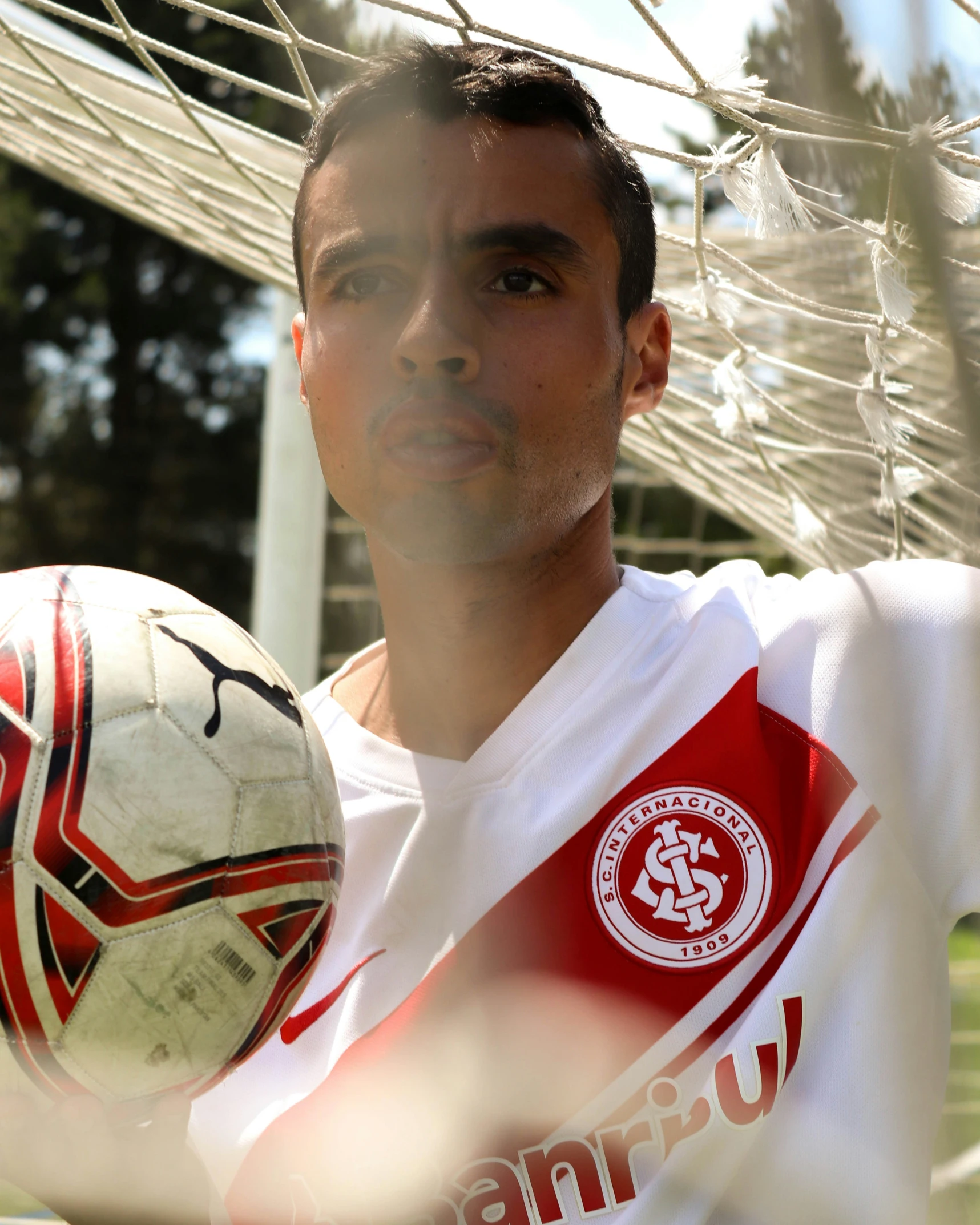 a man with a soccer ball stands at the end of a net