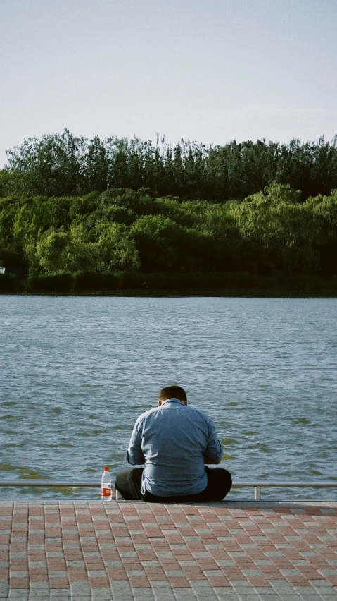 a man sitting down near the water on his knees