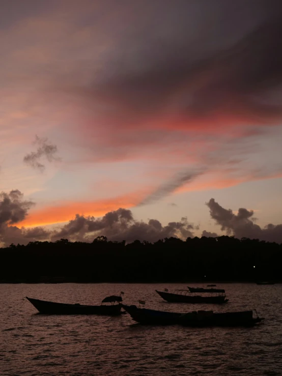 a group of boats floating in the ocean at sunset