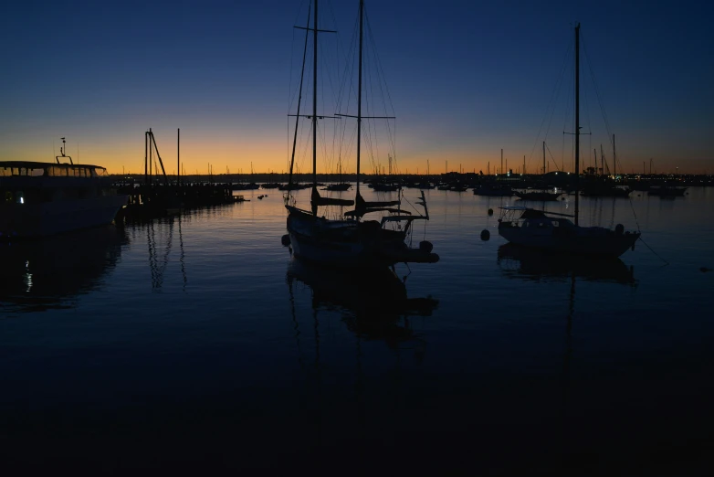 a sunset behind many sail boats on a lake