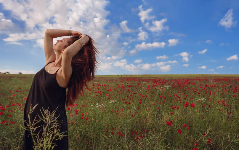 a girl wearing a black dress is standing in a field with red flowers