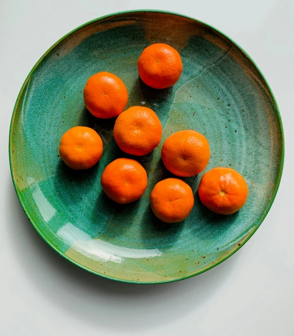 a green bowl full of oranges that are sitting on a table