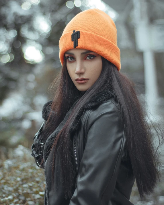 a girl in a leather jacket and hat is wearing a cross beanie