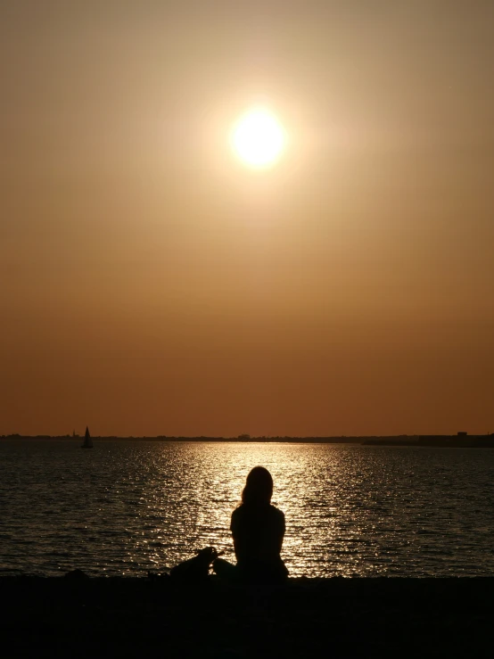 a person sits on the shore watching the sunset