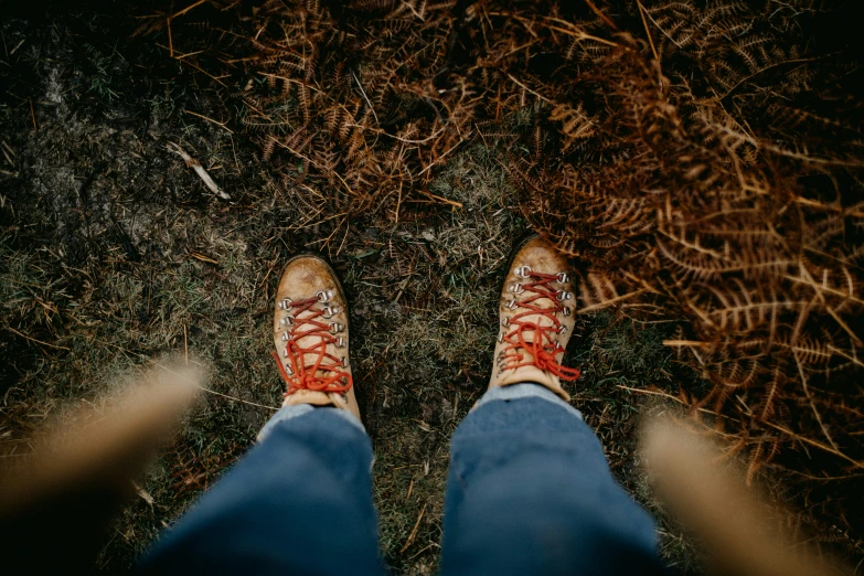 a person wearing blue jeans and brown shoes standing in a field