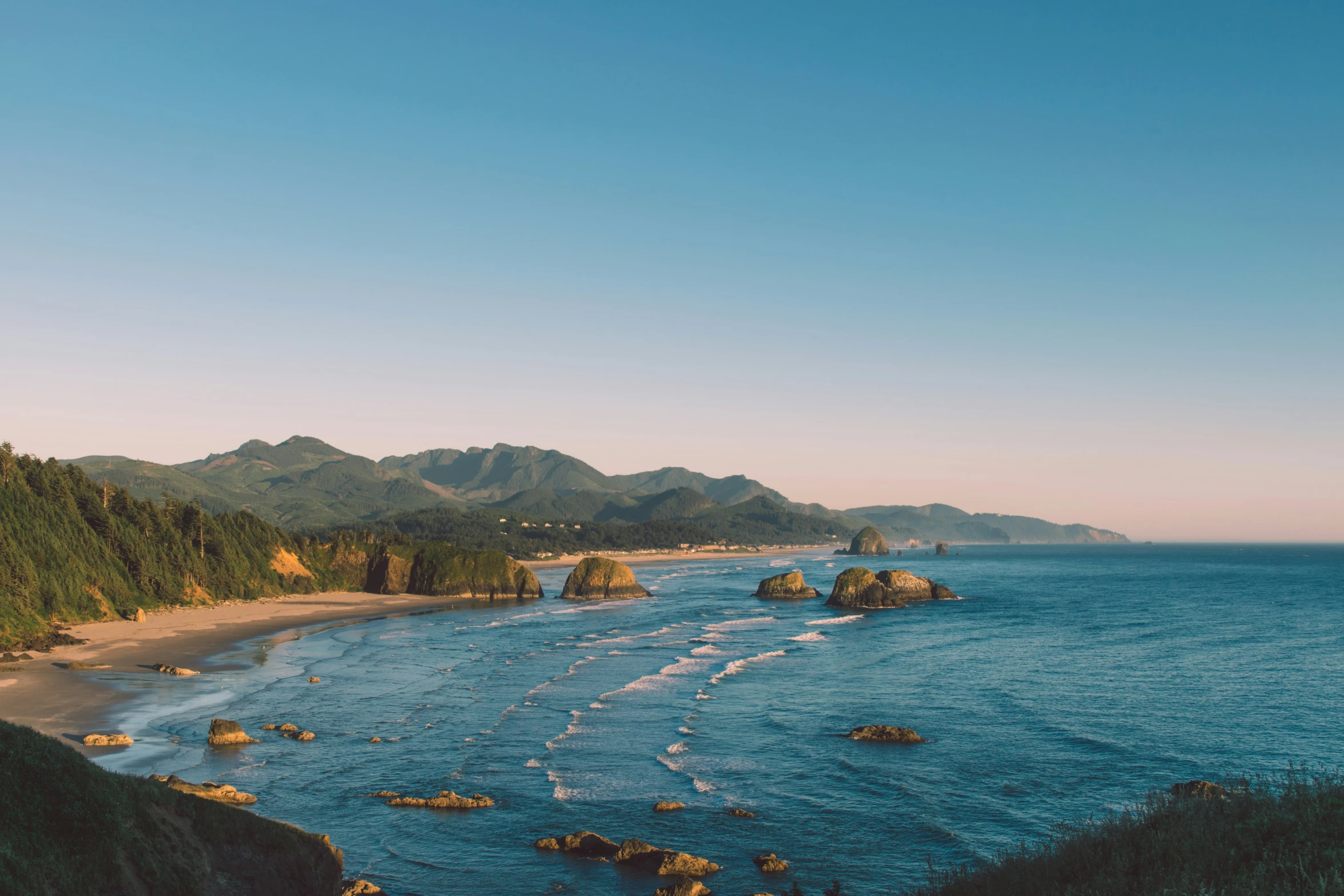 a sandy beach lined with green mountains and clear blue water