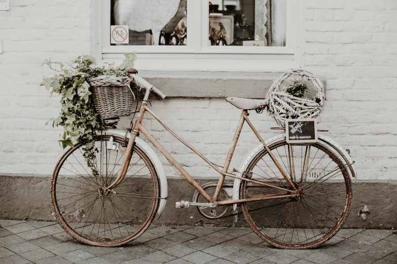 an old bicycle next to a brick wall with plants and a bike basket attached to it