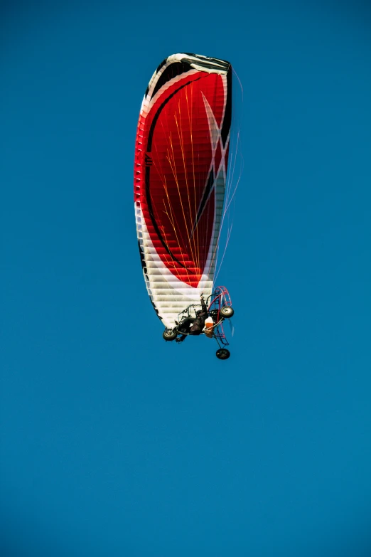a person parasails high in the air against a blue sky