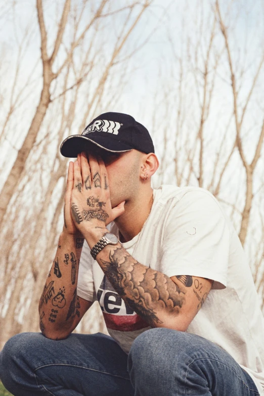 a man wearing tattoos kneeling in a field