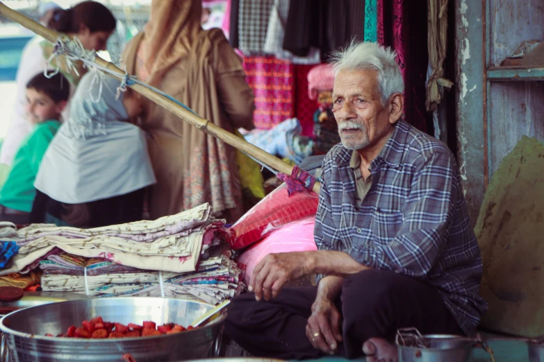 an older man is sitting outside his home selling vegetables