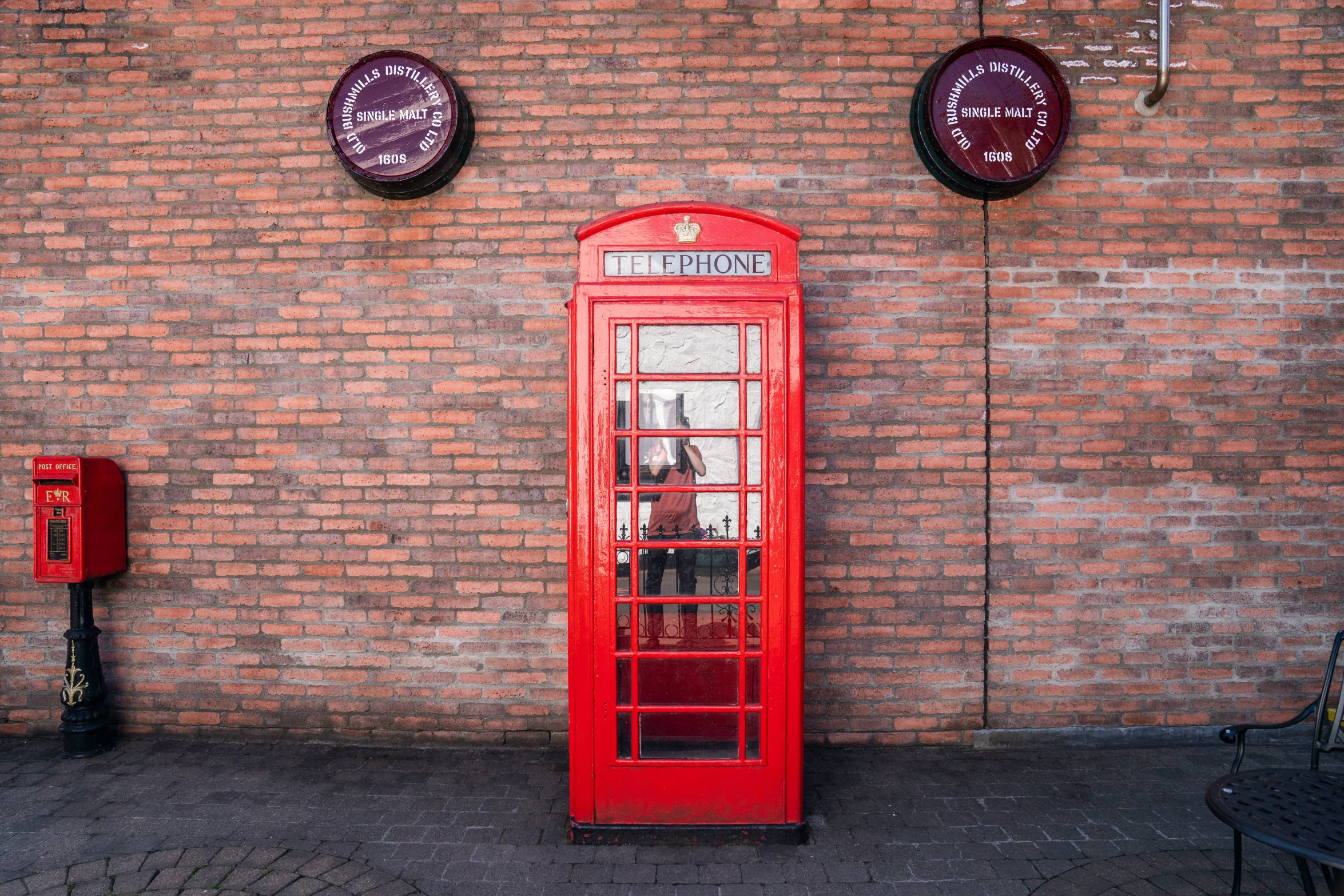 a red telephone booth sitting on the sidewalk in front of a brick wall