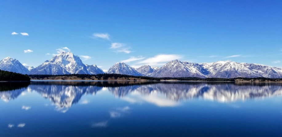 a body of water sitting below mountains under a blue sky