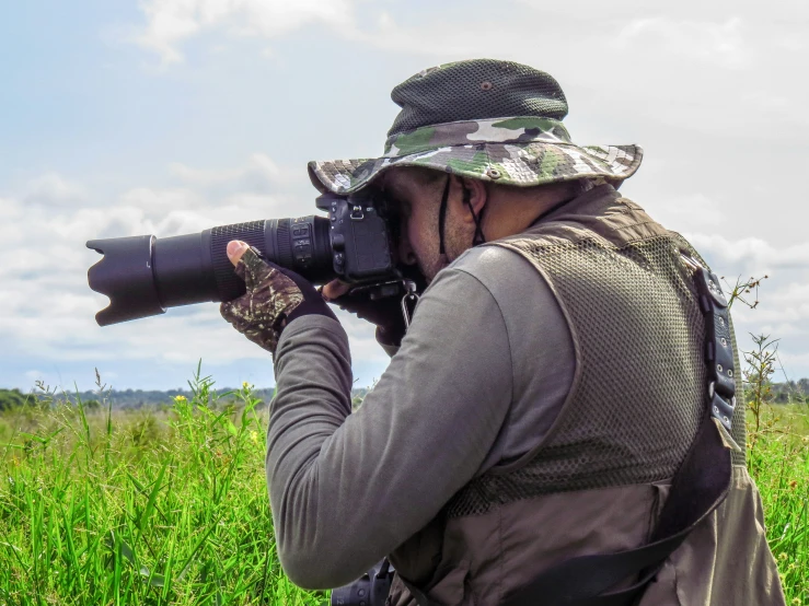 a pographer with binoculars and an umbrella standing in a grassy field