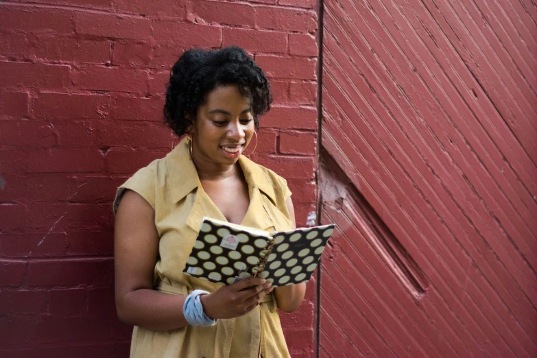 a woman is holding an open book near a brick wall