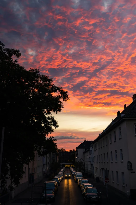 a sunset over a city street with cars parked along side