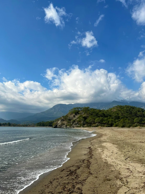 a long sandy beach next to the ocean with some clouds