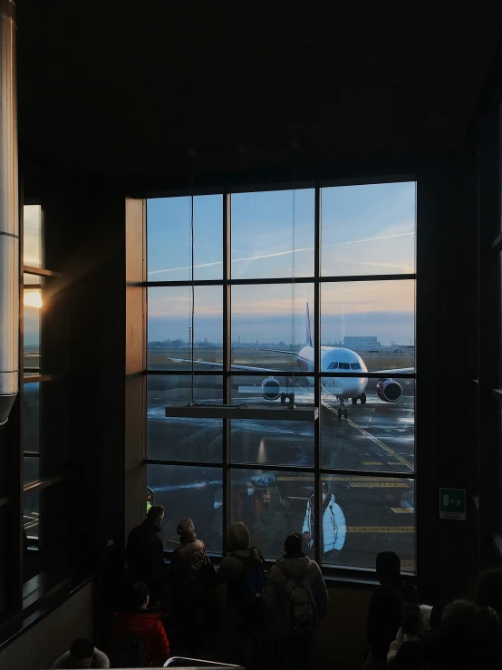 people sitting on chairs looking at an airport plane through a window