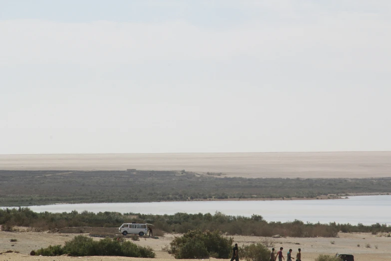 four people are walking along the shoreline, near some water