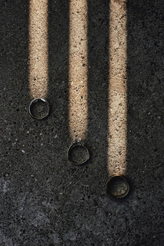 the shadows are cast on cement as a couple of pairs of rings sit on a road