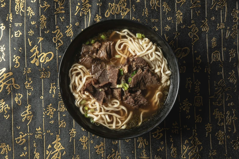 a bowl of noodles with beef and vegetables on a oriental cloth