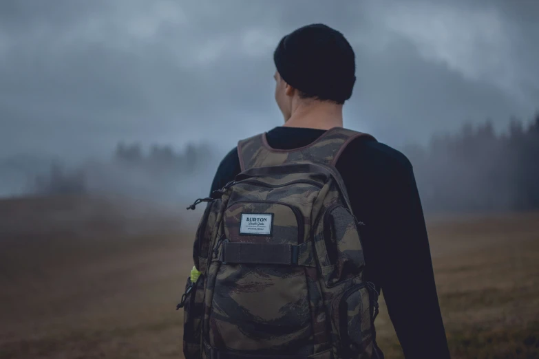 a man stands alone in a field with trees in the background